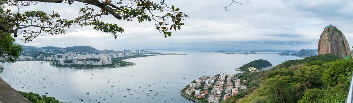 Stunning aerial view of Santos Dumont airport, Sugarloaf Mountain, and vessels in Rio de Janeiro's bay under a beautiful evening sky.