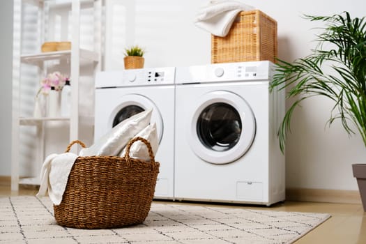 A modern laundry room features two white washing machines, a white shelf unit, a wicker basket, and a potted plant.
