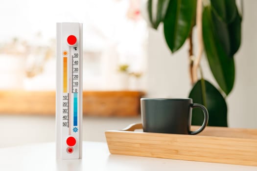 A white thermometer with a red dot at the top and a yellow, orange, and blue scale stands on a white table.