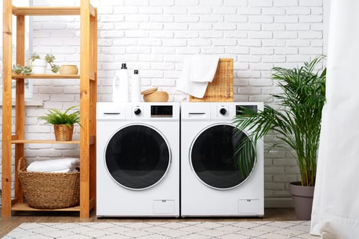 A modern laundry room with white appliances, a wooden shelf, a potted plant, and a white curtain.