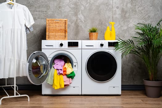 A white front-loading washing machine with the door open, revealing a pile of colorful clothes inside.