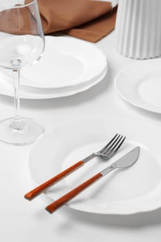 Stylish table setting with white dishware on white tablecloth close up