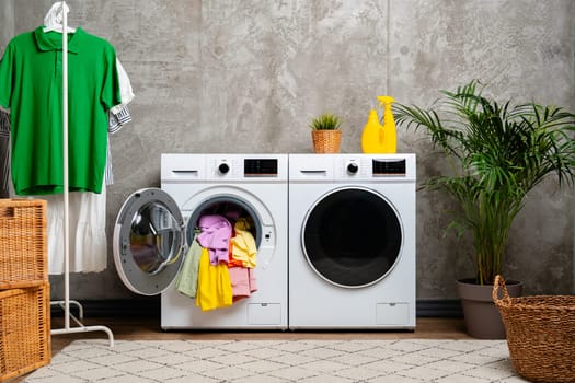 A white front-loading washing machine with the door open, revealing a pile of colorful clothes inside.
