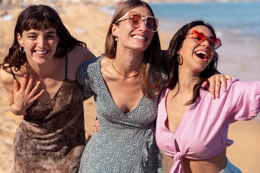 Cheerful multiethnic friends with sunglasses happy on vacation on the beach, looking at the camera.