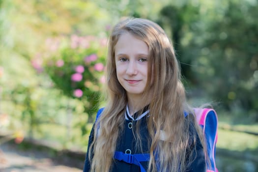 Back to school, portrait of a little girl from primary school outdoors, enjoying flowers in a flowerbed and looking at the camera with a smile, student dressed in dark blue uniform