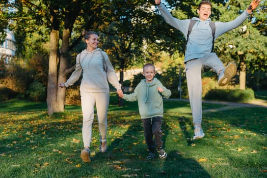 a family mom and 2 sons are having fun, running in the park and jumping. Sons, children, mom, run, play, rejoice, enjoy nature in summer. Family teamwork. Happy family team, running together in field, happily waving their hands. Group of people of different ages. happy family, mom and two sons on an emotional walk. Running and enjoying life in a green field in the park, blue sky, nature.