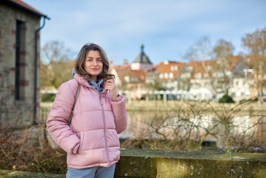 Young beautiful pretty tourist girl in warm hat and coat with backpack walking at cold autumn in Europe city enjoying her travel in Zurich Switzerland. Outdoor portrait of young tourist woman enjoying sightseeing