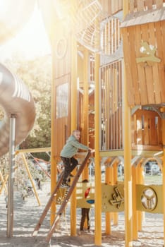 boy playing on the children's playground, a boy on a playground in the park climbs up a climbing wall. Kids having fun and sliding on outdoor playground. Kids Enjoying. A child climbs up an alpine grid in a park on a playground on a hot summer day. children's playground in a public park, entertainment and recreation for children, mountaineering training.