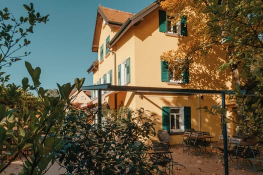 Image of a empty coffee tables arranged in backyard of a house. Autumn in Germany, Europe. Outdoor table in street cafe. autumn outdoor cafe wooden furniture old europe. Autumn photo of old-fashioned cozy and empty outdoor cafe with wooden furniture in a European town. Cafe concept