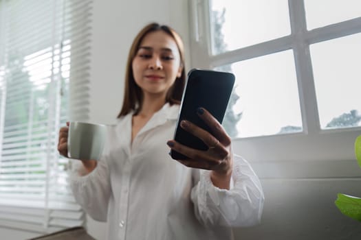 A woman starts her day with a cup of coffee and checks her smartphone by the window in a bright, modern home.