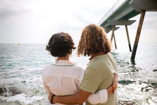 Smiling couple wearing sunglasses enjoying a vacation embracing looking at the sea.