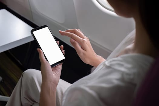 A young businesswoman uses her smartphone while traveling by plane, staying connected and productive during her flight.