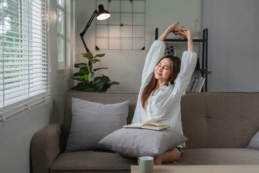 A young woman stretches and relaxes on a comfortable sofa, enjoying her morning routine in a modern and cozy living room.