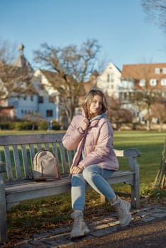 Winter Wonderland Elegance: Beautiful Girl in Pink Jacket Enjoys Festive Atmosphere in Bitigheim-Bissingen Park. Experience the magic of the holiday season as a charming girl in a pink winter jacket sits on a bench in a park against the backdrop of the historic town of Bitigheim-Bissingen, Baden-Württemberg, Germany. The scene is adorned with picturesque half-timbered houses, creating a delightful blend of winter charm and architectural beauty.