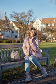 Embrace the tranquility of winter with this captivating image featuring a beautiful girl in a pink winter jacket, leisurely sitting on a bench in a park against the backdrop of a charming old European town. The photograph beautifully captures the serene atmosphere, blending the girl's winter style with the timeless charm of the historic surroundings. Winter Wonderland Elegance: Beautiful Girl in Pink Jacket Enjoys Festive Atmosphere in Bitigheim-Bissingen Park. Experience the magic of the holiday season as a charming girl in a pink winter jacket sits on a bench in a park against the backdrop of the historic town of Bitigheim-Bissingen, Baden-Wurttemberg, Germany. The scene is adorned with picturesque half-timbered houses, creating a delightful blend of winter charm and architectural beauty.