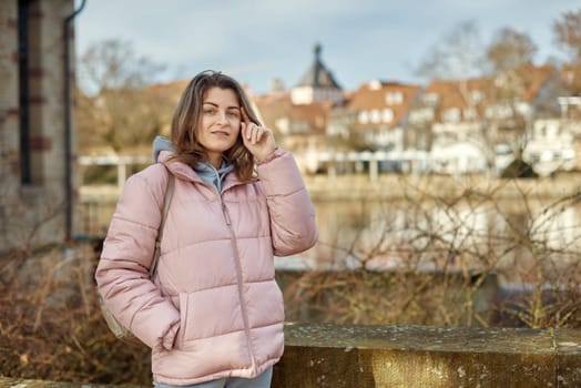 Young beautiful pretty tourist girl in warm hat and coat with backpack walking at cold autumn in Europe city enjoying her travel in Zurich Switzerland. Outdoor portrait of young tourist woman enjoying sightseeing