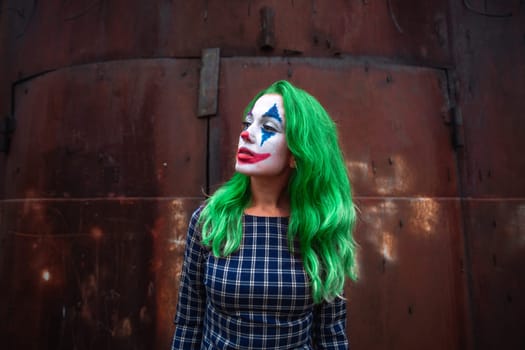 Portrait of a greenhaired girl in chekered dress with joker makeup on a atmospheric rusty metal wall background.