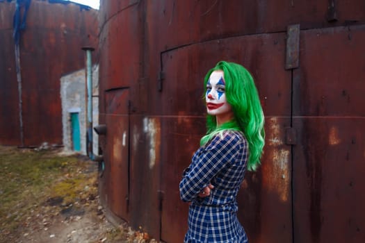 Portrait of a greenhaired girl in chekered dress with joker makeup on a atmospheric rusty metal wall background.