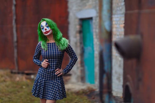 Portrait of a greenhaired girl in chekered dress with joker makeup on a atmospheric rusty metal wall background.