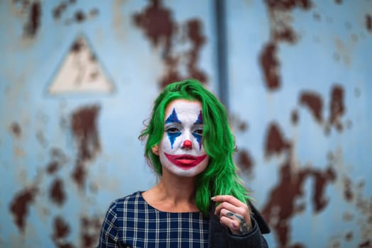 Portrait of a greenhaired girl in chekered dress with joker makeup on a atmospheric rusty metal wall background.