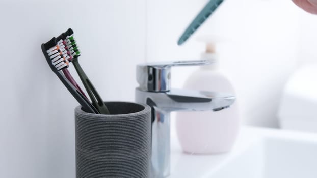 Woman'S Hand Throws Toothbrush Into Glass With 4 Toothbrushes Already In It
