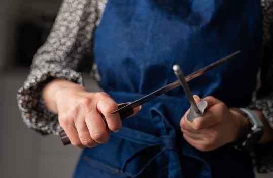 Woman Sharpens Knife In Kitchen Apron, Close-Up Of Hand In Focus