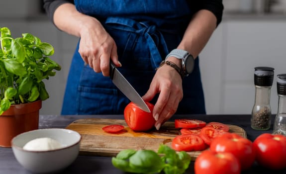 Preparing Caprese Salad, Female Hands Are Cutting Tomatoes On A Board, With Mozzarella, Basil, And Spices Nearby
