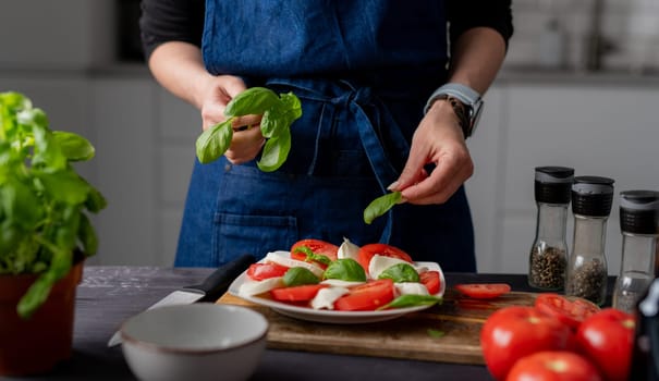 Woman Decorates Caprese Salad With Basil, Made From Tomatoes And Mozzarella Cheese
