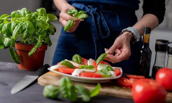 Woman Decorates Caprese Salad With Basil, Made From Tomatoes And Mozzarella Cheese