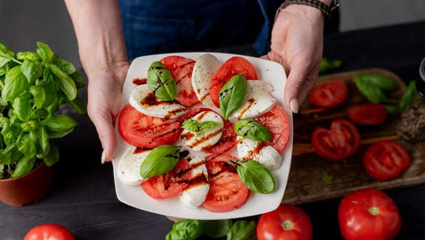 Woman Holds Caprese Salad On Plate, Close-Up Of Tomatoes And Mozzarella Cheese