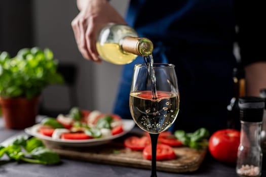 Woman'S Hand Pours Wine Into Glass Against Backdrop Of Caprese Salad, Close-Up View