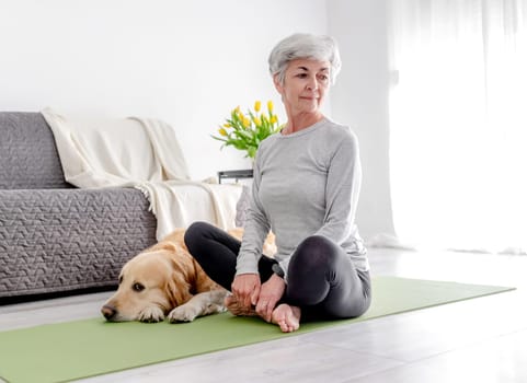 Grey-Haired Retired Woman Practices Yoga At Home Next To Her Golden Retriever Dog