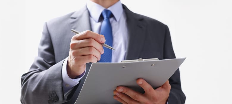 Hand of businessman in suit filling and signing with silver pen partnership agreement form clipped to pad closeup. Management training course some important document team leader ambition concept