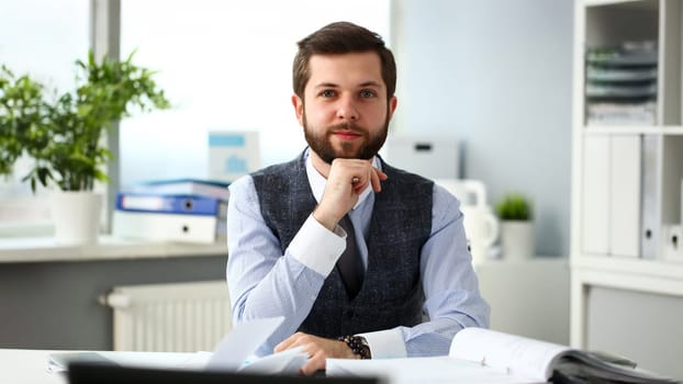Handsome smiling bearded clerk man at office workplace with silver pen in arms do paperwork portrait. Staff dress code worker job offer client visit study profession boss stock idea coach training
