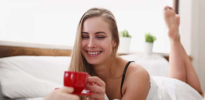 young pretty blond woman have cup of tea coffee early morning in her bed