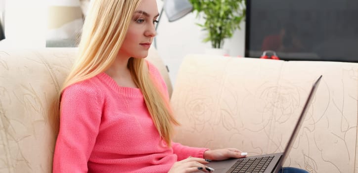 young beautiful blond woman sit on the sofa in livingroom hold laptop in arms sunny morning concept