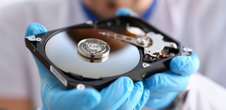 A male repairman wearing blue gloves is holding a hard drive from computer or laptop in hands. Performs fault diagnostics and performs urgent repairs recovery of lost data during deletion HDD closeup