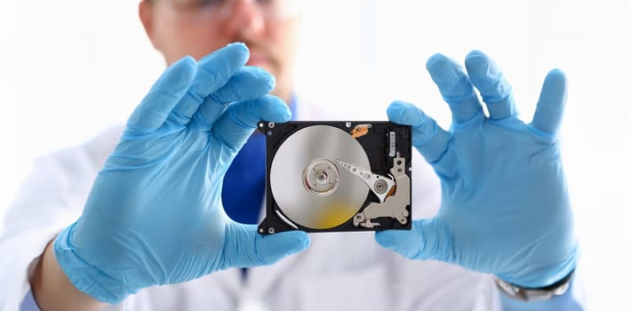 A male repairman wearing blue gloves is holding a hard drive from computer or laptop in hands. Performs fault diagnostics and performs urgent repairs recovery of lost data during deletion HDD closeup