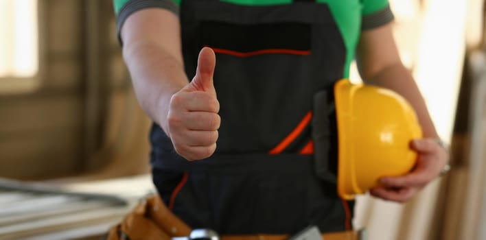 Hand of worker in yellow helmet show confirm sign with thumb up at arm portrait. Manual job DIY inspiration joinery startup idea fix shop hard hat industrial education profession career concept