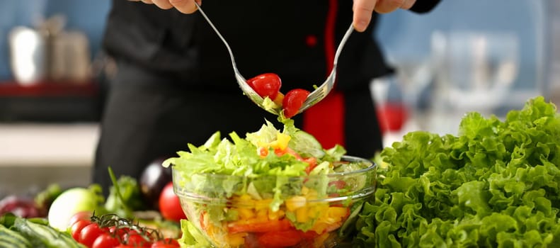 Cook holds fork in hand and mixes salad fresh vegetables seasoned with olive oil. Raw food and vegetarian in modern society is popular concept.