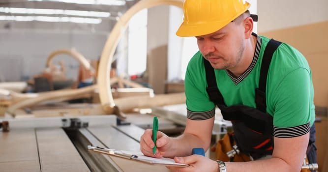 Portrait of young attractive man in work clothes and yellow helmet crossed arms smiling at shop for manufacturing furniture and details home interior