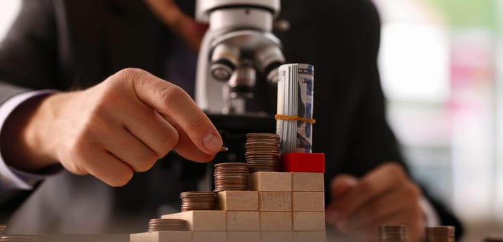 Hand businessman in suit hold quarter in background looking through microscope closeup search business concept