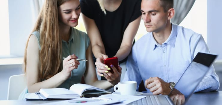 A group of people in a cafe communicate with a cup of coffee looking at the smartphone app and photos from the vacation