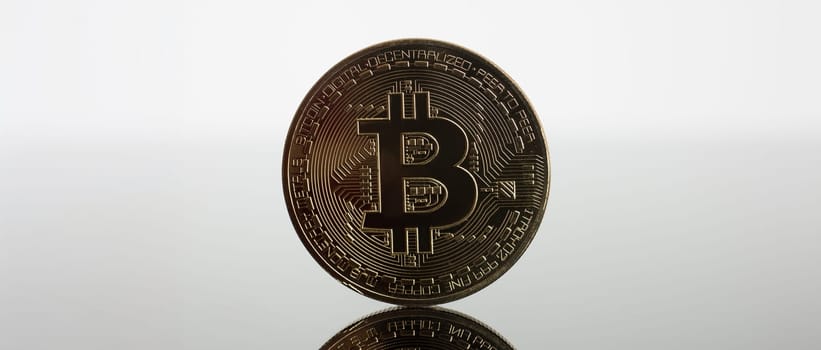 Coin of crypto currency bitcoin on a gray-blue background with reflection subject gold exchange pyramid on money in connection with the growth or fall exchange rate closeup.