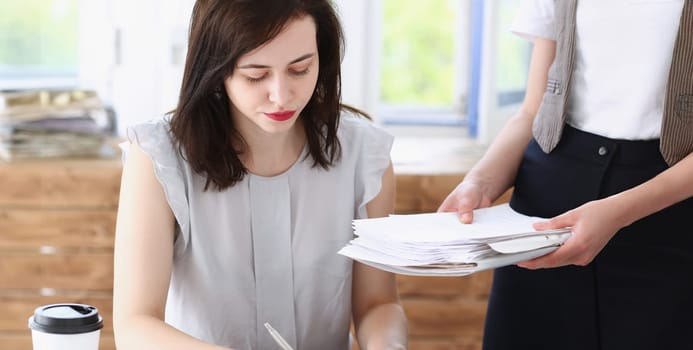 Female employee show pack of documents to busy male manager or boss give extra work to executor. White collar portrait contract approval headache and depression irs lot of new problems concept