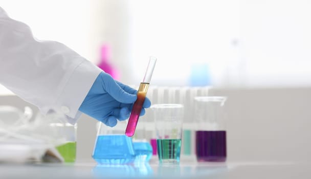 A male chemist holds test tube of glass in his hand overflows a liquid solution of potassium permanganate conducts an analysis reaction takes various versions of reagents using chemical manufacturing.