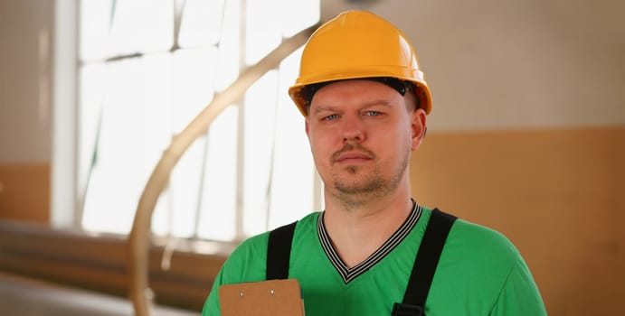 Portrait of young attractive man in work clothes and yellow helmet crossed arms smiling at shop for manufacturing furniture and details home interior