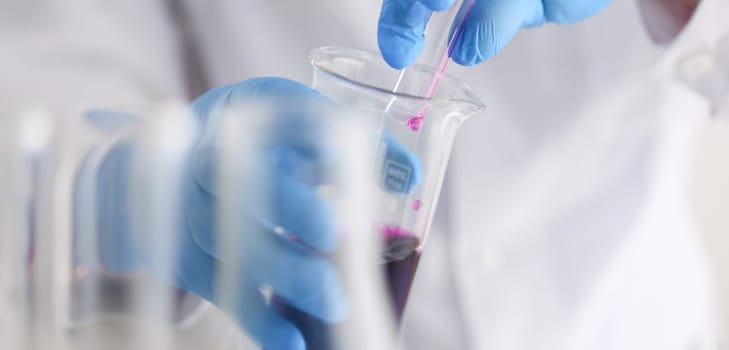 A male chemist holds test tube of glass in his hand overflows a liquid solution of potassium permanganate conducts an analysis reaction takes various versions of reagents using chemical manufacturing.