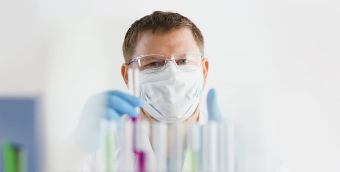 A portrait of a young surgeon chemist doctor looks at a container with a blue liquid and a mask is fought with viruses and a vaccine for vaccines against diseases.