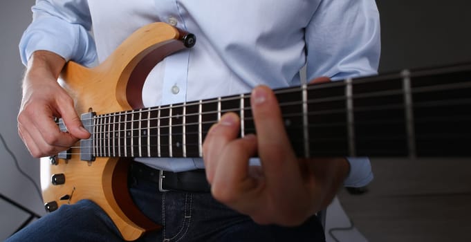 Male arms holding and playing classic shape wooden electric guitar closeup. Six stringed learning musical school education art leisure electrical vintage stage shop having fun enjoying hobby concept